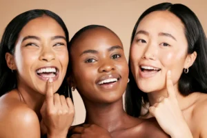 Três mulheres sorrindo, com pele bem cuidada e uniforme, em foto promocional que ilustra dicas sobre como saber qual meu tipo de pele e identificar características faciais