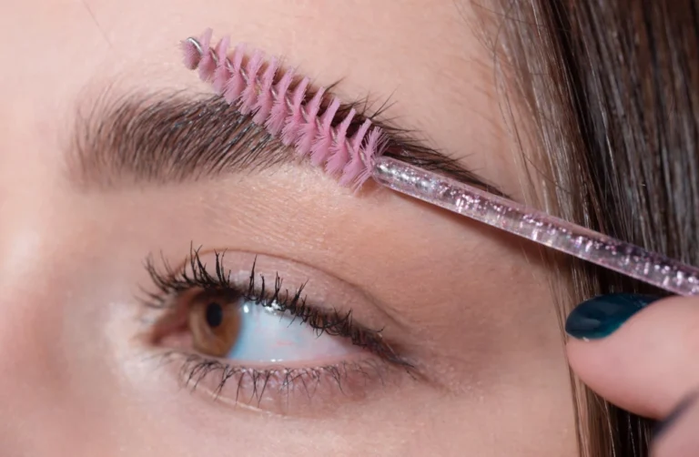 Aplicação de rímel transparente nos cílios, destacando a definição e volume natural, com foco na escovinha rosa para máscara de cílios transparente.