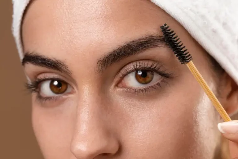 Mulher usando gel para sobrancelha para definir e manter a forma dos pelos, com aplicador na sobrancelha e cabelo coberto por touca branca.
