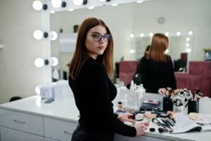 fornecedor de maquiagem: Profissional de maquiagem em estúdio, com pinceis e cosméticos organizados na bancada diante do espelho iluminado. Atendimento e preparo para make.