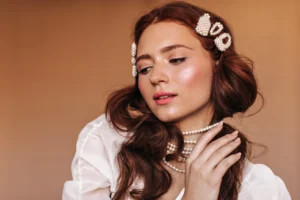 Mulher com maquiagem romântica em tons suaves, pele iluminada e batom rosado, usando acessórios em pérolas no cabelo e na orelha, ideal como maquiagem para o dia dos namorados.
