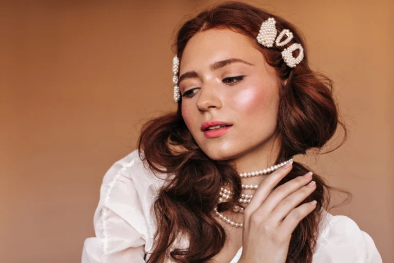 Mulher com maquiagem romântica em tons suaves, pele iluminada e batom rosado, usando acessórios em pérolas no cabelo e na orelha, ideal como maquiagem para o dia dos namorados.