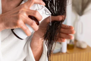 Pessoa aplicando tratamento capilar no cabelo úmido com produtos para cabelo, como spray, cuidando da saúde e beleza dos fios.
