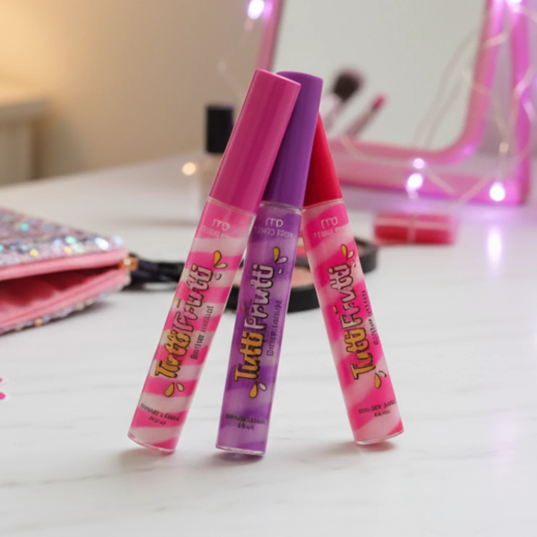 Três gloss de boca nas cores rosa, roxo e vermelho, posicionados na mesa com fundo delicado de maquiagem e espelho rosa, ideal para quem procura marcas de cosmético para revender