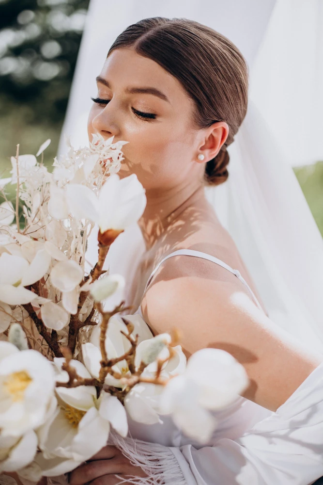 Fotografia de uma noiva com maquiagem impecável, olhos fechados e segurando um buquê de flores brancas, ideal para quem busca inspiração em maquiagem para noiva.
