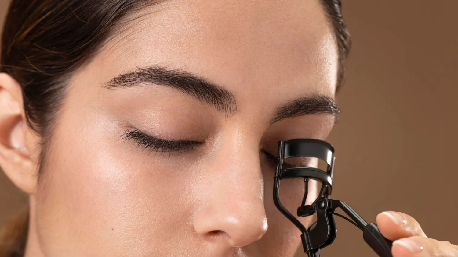 Aplicação de mascara de cilios incolor e rímel incolor com curvex na região dos cílios, mostrando a preparação da maquiagem em close no rosto de uma mulher.