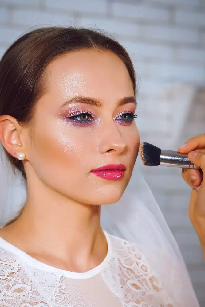 Mulher recebendo maquiagem para noiva com blush e maquiagem bem feita no rosto, com foco na aplicação do blush na bochecha.