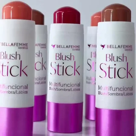 Imagem com três batons em bastão da marca BELLA FEMME, com embalagens em tons roxo e vermelho. Nos rótulos aparece “Blush Stick” e “Multifuncional”, sugerindo produto para blush, contorno e aplicação em rosto.