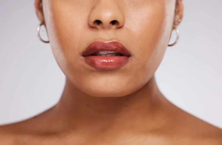 Close-up de lábios com acabamento lip glow em tom rosado e brilho suave, destacando a boca e o contorno em maquiagem com efeito iluminado