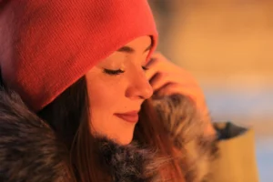 Mulher usando gorro vermelho e casaco com pele exposta ao frio no inverno, com olhar sereno e luz quente ao ar livre, transmitindo cuidados com pele no inverno e hidratação