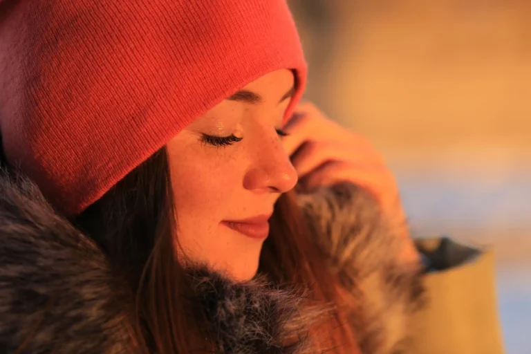 Mulher usando gorro vermelho e casaco com pele exposta ao frio no inverno, com olhar sereno e luz quente ao ar livre, transmitindo cuidados com pele no inverno e hidratação