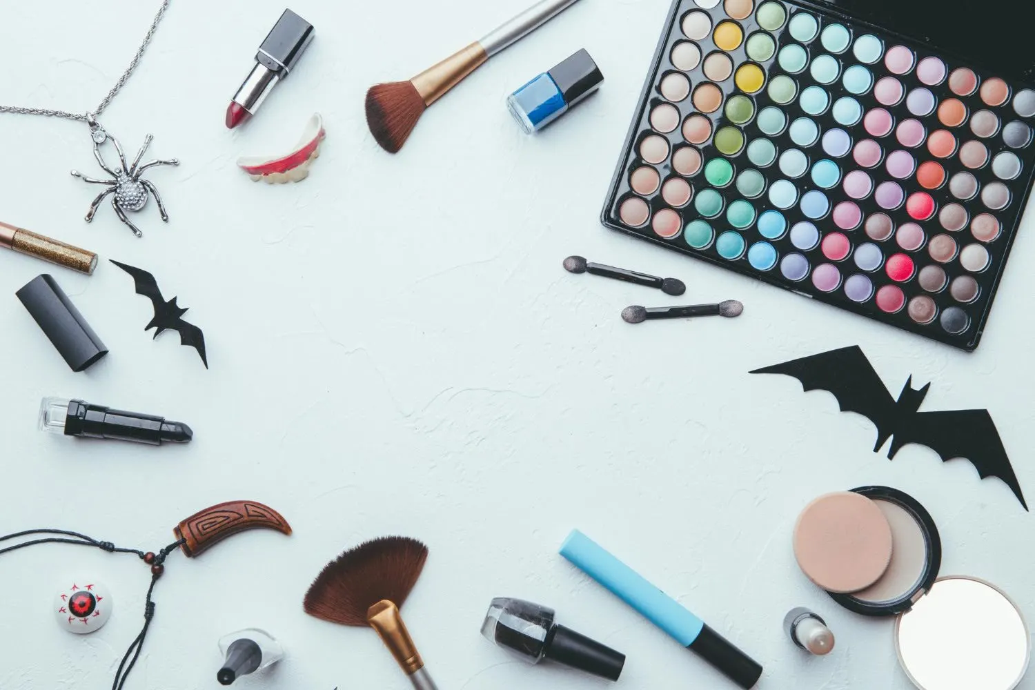 Materiais de maquiagem e beleza sobre fundo branco com acessórios temáticos de Halloween e Dia das Crianças, como bat e esmaltes coloridos.