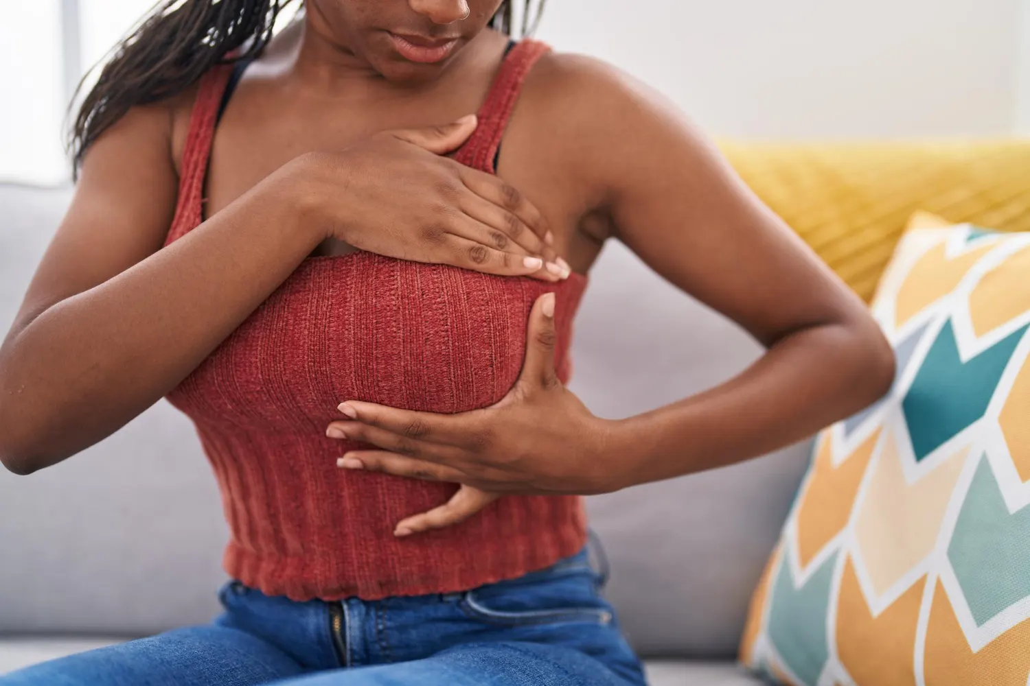 Mulher com roupa rosa segurando a própria mama enquanto recebe cuidado e carinho no sofá, mensagem relacionada ao outubro rosa